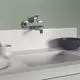 Küchenarmatur von Ideal Standard, Wandmontage, in Chrom. Die Armatur ist an einer hellen Arbeitsplatte installiert, neben einem schwarzen Gefäß und einem Stapel Teller.
